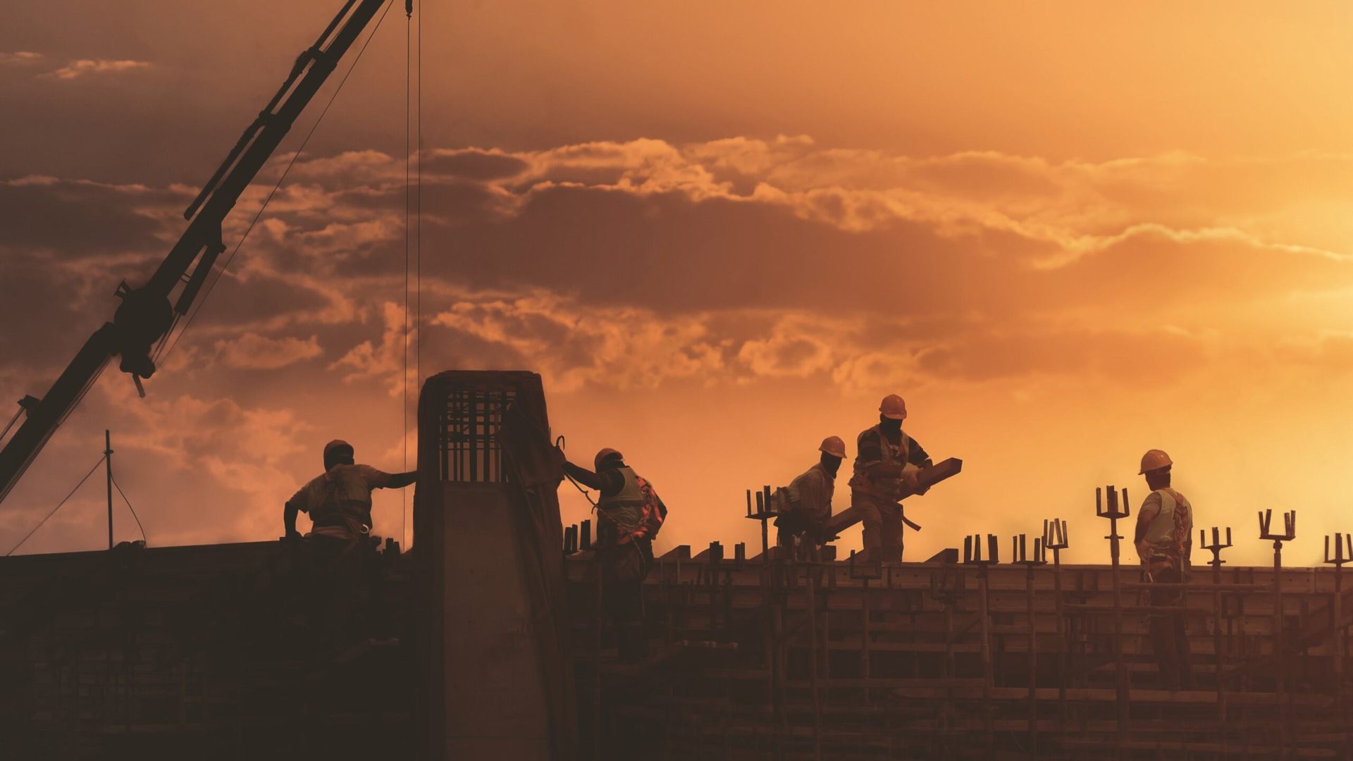 Construction workers in silhouette against orange sunset